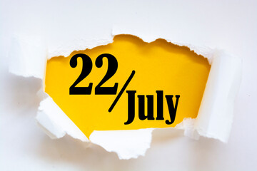 July 22. 22th day of the month, calendar date. Hole in paper with edges torn off. Yellow background is visible through ragged hole. Summer month, day of the year concept.