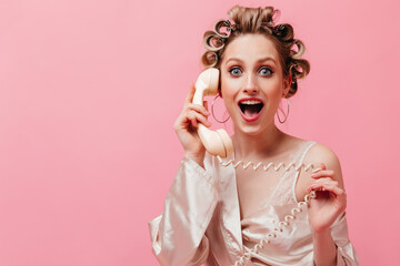 Enthusiastic girl in pink robe happily talking on phone and posing on isolated background.