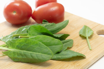Sorrel lies on a cutting board close-up on a white background, and vegetables-tomatoes in the background.