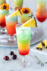 close up view of a tall frosty glass of a colourful cocktail with other cocktails in behind.