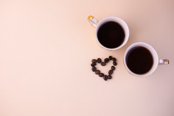 Two cups of coffee with the heart made of coffee beans on a light beige background