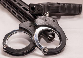 Obraz premium A pair of black and silver handcuffs laying over the barrel of an AR 15 rifle with a black 9mm pistol on top of them on a white background