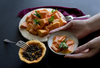 Woman's hands serve plates with fruits. Sliced papaya on plate. Tropical fruit