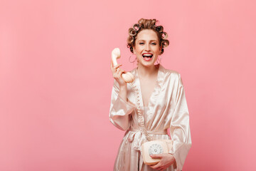 Mischievous girl in silk robe is laughing. Housewife with hair curlers talking on phone.