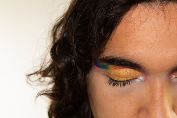 close up of the face of a gay hispanic man with rainbow makeup on a white background