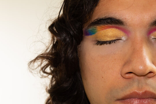 close up of the face of a gay hispanic man with rainbow makeup on a white background
