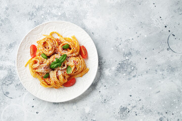 Tasty appetizing classic italian tagliatelle pasta with tomato sauce, cheese parmesan and basil on plate on light table. View from above, horizontal. Top view with copy space