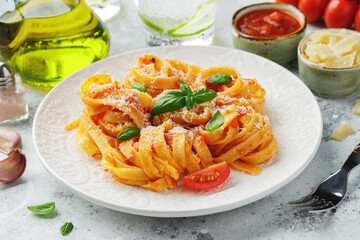 Tasty appetizing classic italian tagliatelle pasta with tomato sauce, cheese parmesan and basil on plate on light table. View from above, horizontal