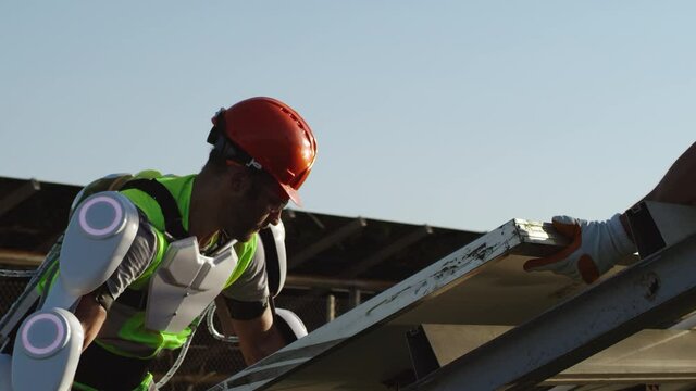Male technician in exoskeleton installing solar cell with colleague