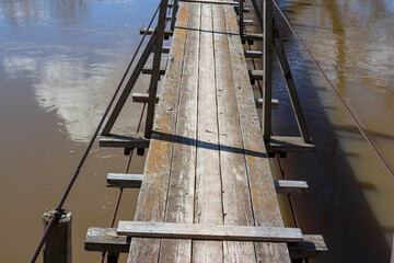 Obraz premium Suspended pedestrian bridge over the river with wooden deck