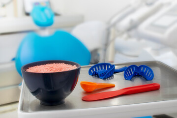 Dental concept of Alginate teeth impressions. There is a cup with Alginate over a dental chair tray with a spoon a spatula and two impression trays