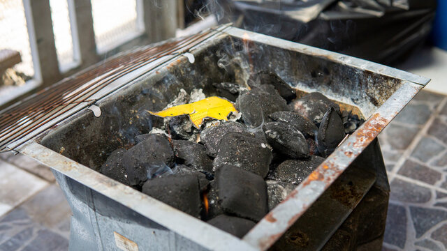 A glowing piles of charcoal briquettes using fire starter inside of black portable mini picnic barbeque grill box. BBQ preparation.