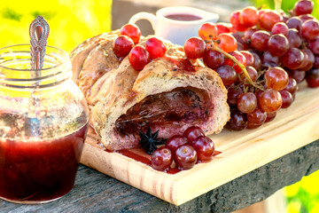 Bread stuffed with grapes jam with some grapes fruits, syrup and jar of jam over wood boards. With copy space and green blurred background