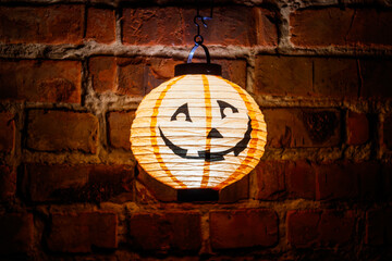 Fototapeta na wymiar Smiling glowing jack-o-lantern hanging on old red brick wall at night. Halloween decoration concept