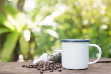 white enamel coffee mug on the old wooden table green forest bokeh background