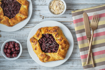 Delicious biscuit with red cherries and almond chips in a white plate on a wooden table, close up
