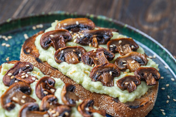 Tasty sandwich with green mashed avocado, fried mushrooms and sesame seeds in