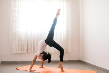 Niña mexicana practicando yoga sobre un tapete naranja a contraluz