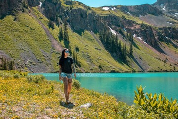 View of a woman with tattoos walking alongside the turquoise water of blue lake in Colorado. This is an alpine lake located along the Blue Lakes Trail.