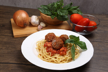 Cooked spaghetti sauce meat ball cheese powder on white plate with ingredients roma tomato glass bowl basil onion garlic wooden board recipe on table marble wall