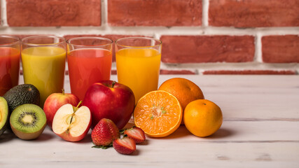Different fruits juice in glass, apple, orange and strawberry juice with straw, looking refreshing on colourful wood board in front of brick wall background. Picture decorating with fresh fruits
