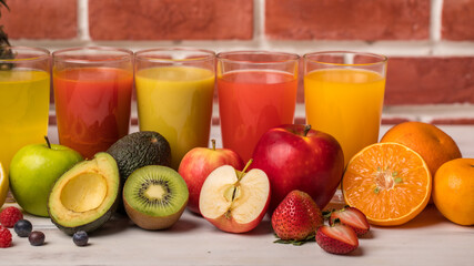 Different fruits juice in glass, apple, orange and strawberry juice with straw, looking refreshing on colourful wood board in front of brick wall background. Picture decorating with fresh fruits