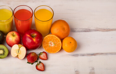 Different fruits juice in glass, apple, orange and strawberry juice with straw, looking refreshing on colourful wood board in front of white wall background. Picture decorating with fresh fruits