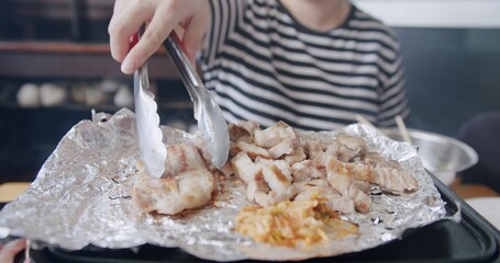 Asian woman grilling roasting sliced meat pork on stove with vegetables on wooden table, Korean style grill meat	
