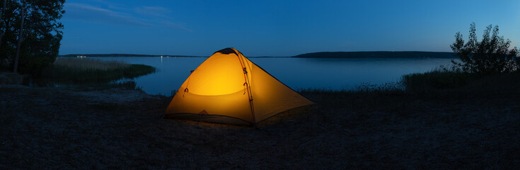 Orange illuminated tourist tent on lake in evening © alexlukin