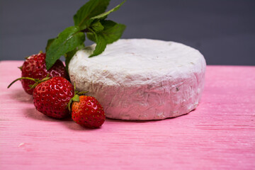 Camembert with strawberries with mint on a pink wooden board on a grey background 