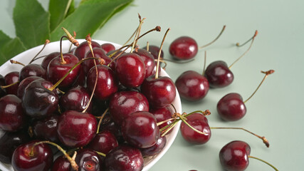 Ripe red cherries in a bowl on green background.