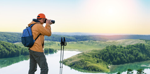 Man hiker taking photo on top of mountain at sunset. Banner.