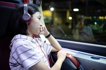 Unhappy asian schoolgirl sit in the bus alone at night,looking through the window,thinking lonely,missing family during back to school,student going to boarding school,homesickness,nostalgia concept