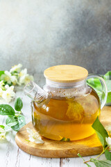 Therapeutic herbal tea. Hot Jasmine tea with jasmine flowers in a glass teapot on a rustic wooden table. Copy space.