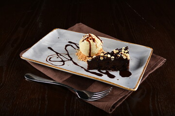 dark chocolate brownie with vanilla ice cream dessert with peanut and chocolate sauce on plate in dark background western halal menu