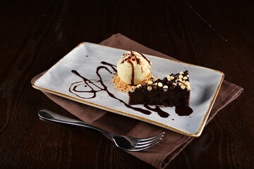 dark chocolate brownie with vanilla ice cream dessert with peanut and chocolate sauce on plate in dark background western halal menu