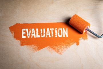 EVALUATION. Paint roller with orange color on a wooden background