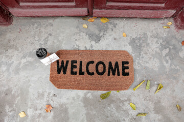 Doormat with cup of coffee and letter near entrance of house on autumn day