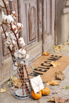 Doormat with cotton flowers and letter near entrance of house on autumn day