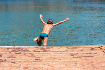 Fototapeta na wymiar happy boy jumping from a bridge into the sea, vacation horizontal.