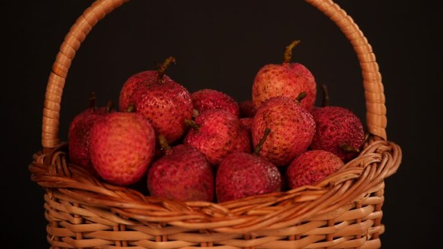 Female hand keeping a peeled Lychee with the unpeeled ones in a basket. Closeup shot of red juicy leeches kept together in a bamboo basket against a black background - nutritious fruit