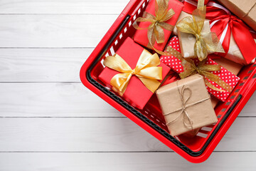 Shopping basket with gift boxes on white wooden background