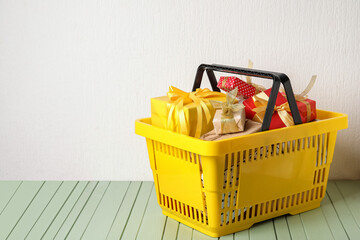 Fototapeta premium Yellow shopping basket filled with assorted wrapped gift boxes on a light green wooden table, holiday season presents, a bright yellow shopping basket is filled with various wrapped gift boxes