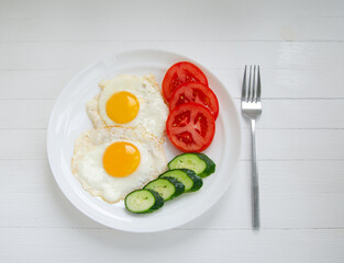 Scrambled eggs from two eggs on a white plate with vegetables. Healthy breakfast on a white background
