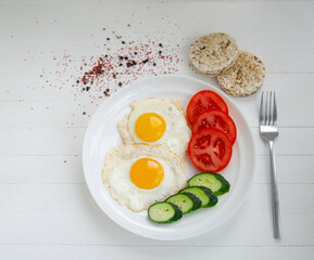 Scrambled eggs from two eggs on a white plate with vegetables. Healthy breakfast on a white background