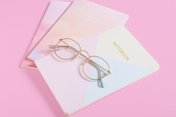 Stylish eyeglasses with notebooks on color background