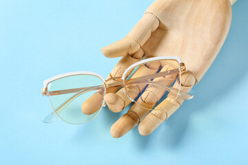 Wooden hand with stylish eyeglasses on color background, closeup