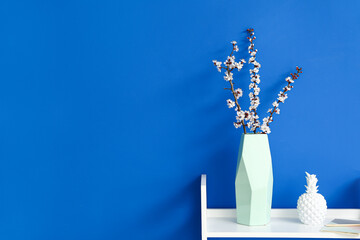 Vase with blooming spring branches on table near color wall