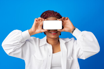 Young afro woman showing blank smartphone screen against blue background