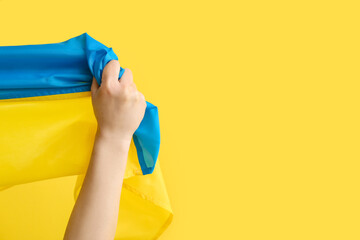 Female hand with flag of Ukraine on color background